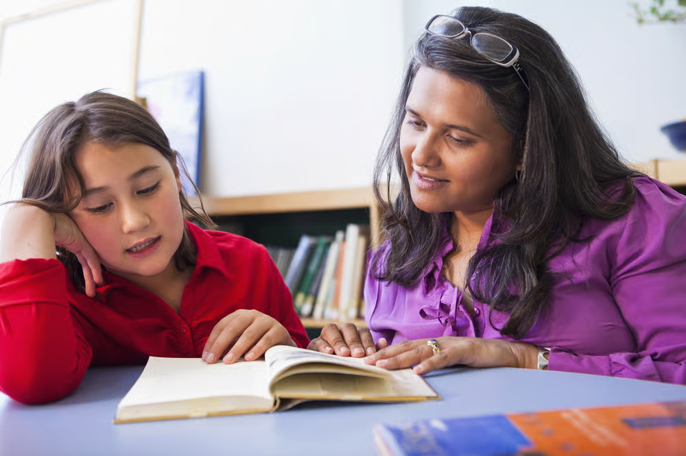 A facilitator and a learner reading a book together at a table